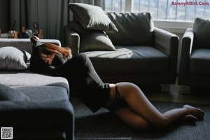 A woman wearing a black mask sitting on a couch.