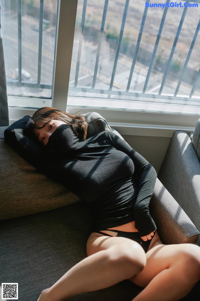 A woman laying on a couch in front of a window.