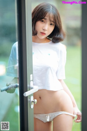 A woman in a white shirt and panties leaning against a window.