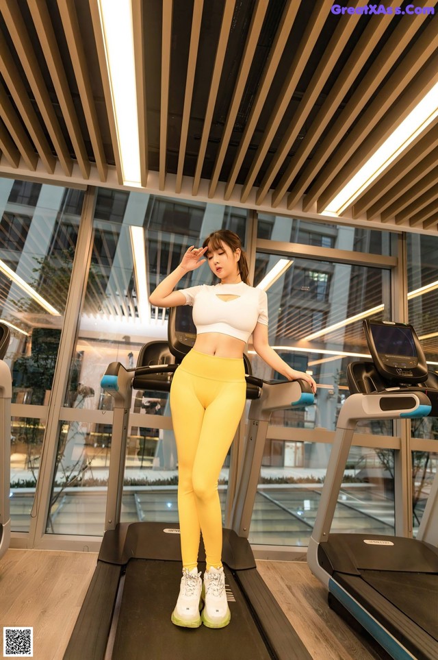 A woman in a white top and yellow leggings on a treadmill.