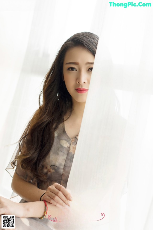 A woman with long brown hair sitting in front of a window.