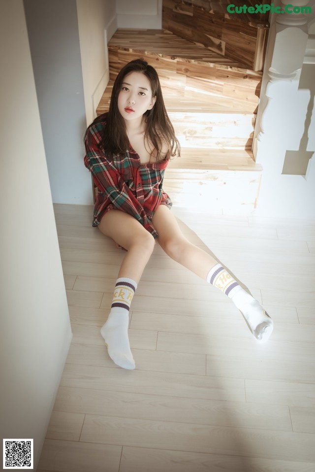A woman sitting on the floor wearing a plaid shirt and socks.