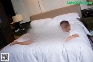 A woman in a white bodysuit sitting on a bed.