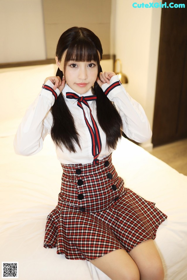 A woman in a school uniform sitting on a bed.