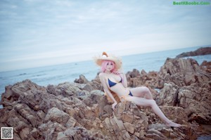 A woman with pink hair sitting on a rock by the ocean.