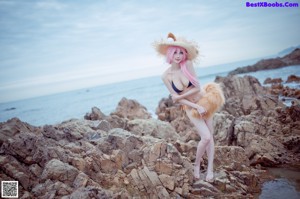 A woman with pink hair wearing a straw hat on the beach.