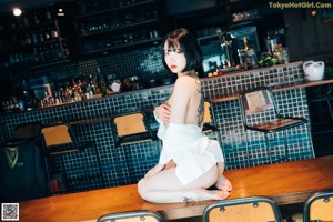 A woman standing behind a bar with bottles of alcohol.