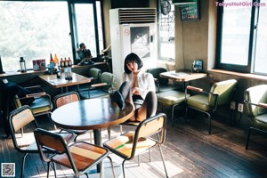 A woman in a white shirt and black skirt holding a bottle of beer.