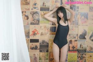 A woman in a black bathing suit standing in front of a wall of posters.
