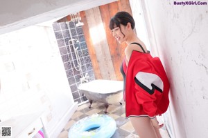 A woman in a black and red swimsuit leaning against a wall.
