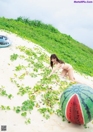 A woman in a pink bikini leaning on a log on the beach.